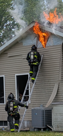Firefighter Daniel Cronk on ladder preparing to ventilate the side of the house